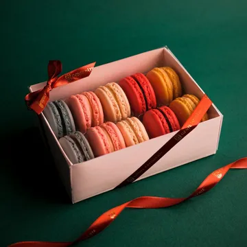 Caixa de presente Génie aberta, com macarons coloridos e fita vermelha.